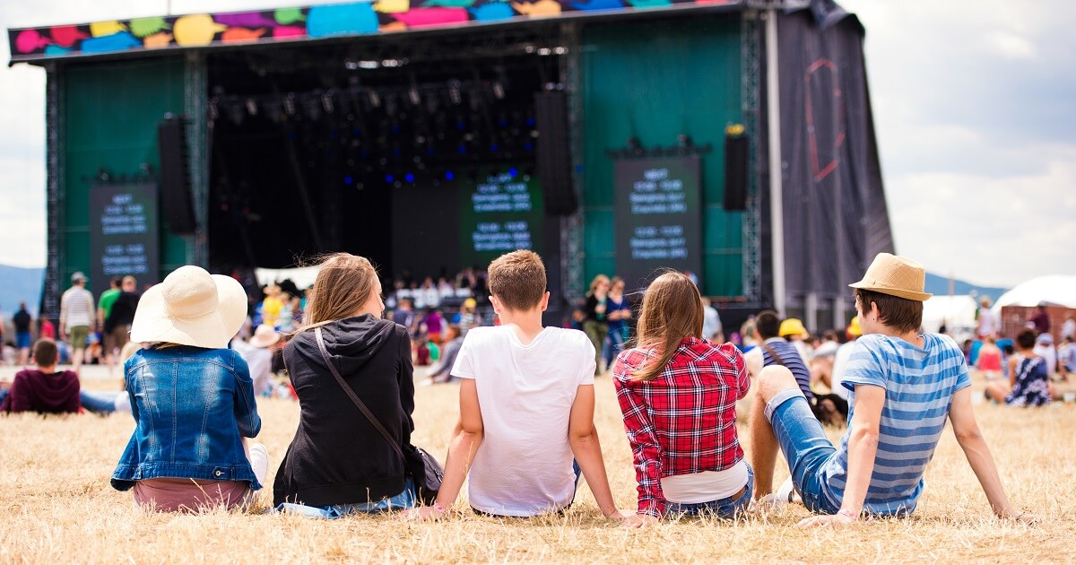 @shutterstock_422373562 Fünf Kinder sitzen auf einem Feld vor einer Bühne