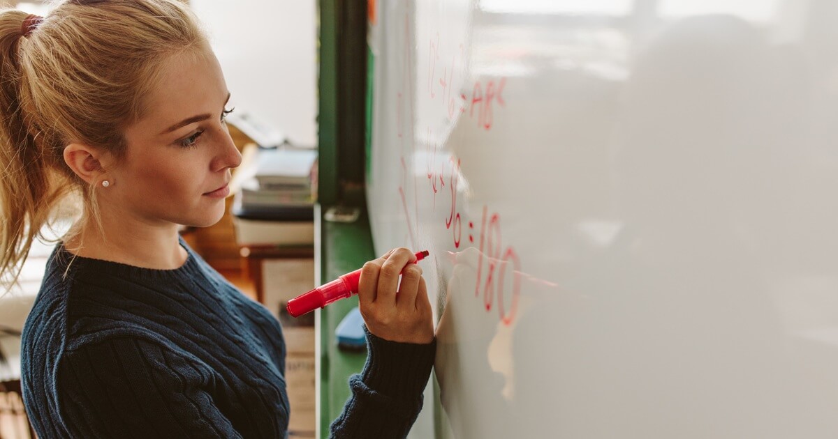 Abiturientin bearbeitet Mathe-Aufgabe an einer Tafel